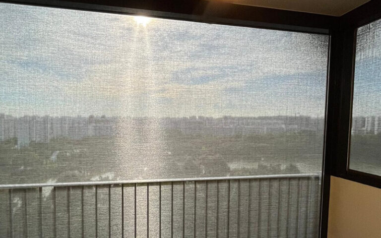 Outdoor balcony roller blind reducing sun glare in high-rise apartment.